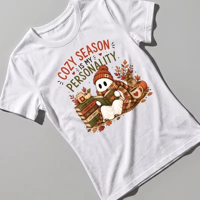 Whimsical illustration of a cute ghost reading with cozy season text — printed on a women's shirt