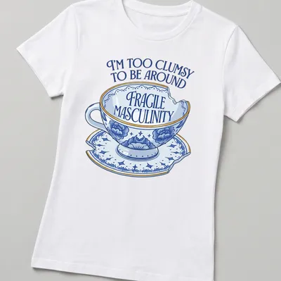 Whimsical illustration of a broken teacup with humorous text about masculinity — printed on a women's shirt