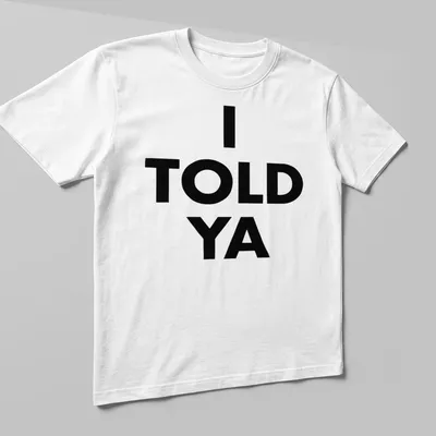 Bold typography t-shirt with the text 'I TOLD YA' in black and white — printed on a unisex t-shirt (angled view)
