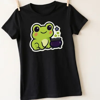 Kawaii frog next to a bubbling cauldron in green, black, purple, and white — printed on a women's shirt