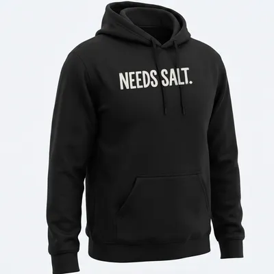 Bold distressed chef graphic with the text 'NEEDS SALT.' in white and light beige — printed on a unisex hoodie