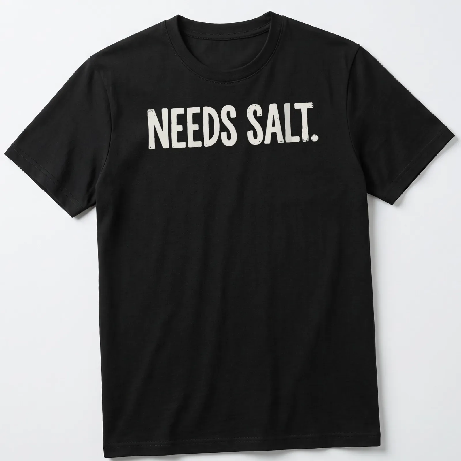 Bold distressed chef graphic with the text 'NEEDS SALT.' in white and light beige — printed on a unisex t-shirt