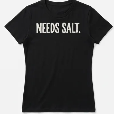 Bold distressed chef graphic with the text 'NEEDS SALT.' in white and light beige — printed on a women's shirt