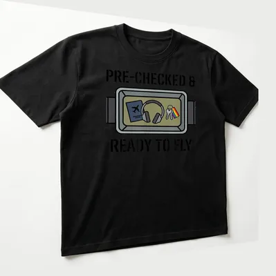 Cartoon illustration of travel essentials with pride flag and text 'PRE-CHECKED & READY TO FLY' — printed on a unisex t-shirt (angled view)