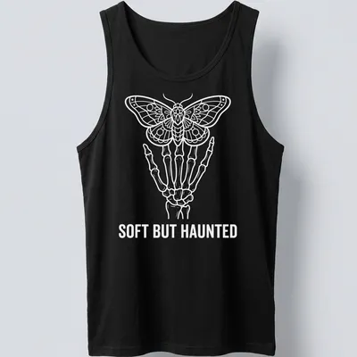 Line art of a skeleton hand holding a moth with the text 'SOFT BUT HAUNTED' in white. — printed on a tank top
