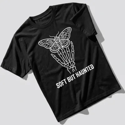 Line art of a skeleton hand holding a moth with the text 'SOFT BUT HAUNTED' in white.