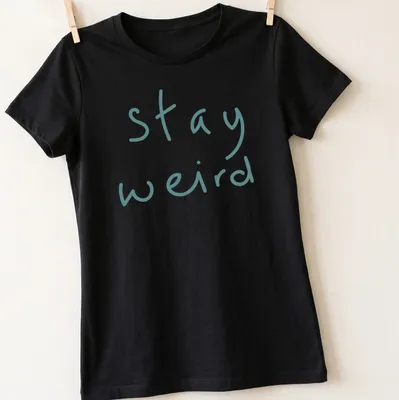 Playful handwritten text 'stay weird' in teal on a t-shirt. — printed on a women's shirt