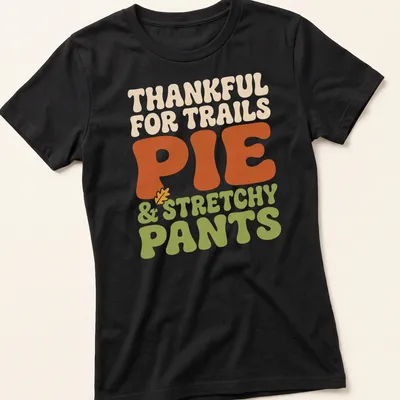 Text-based design celebrating trails, pie, and stretchy pants in retro bold font — printed on a women's shirt