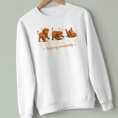 Cartoon Highland cow with the text 'WALKING BY FAITH tripping constantly' in playful colors — printed on a unisex sweatshirt