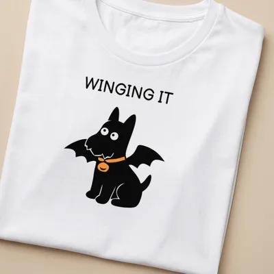 Cartoon Scottish Terrier with bat wings and the text WINGING IT in orange and black — printed on a women's shirt